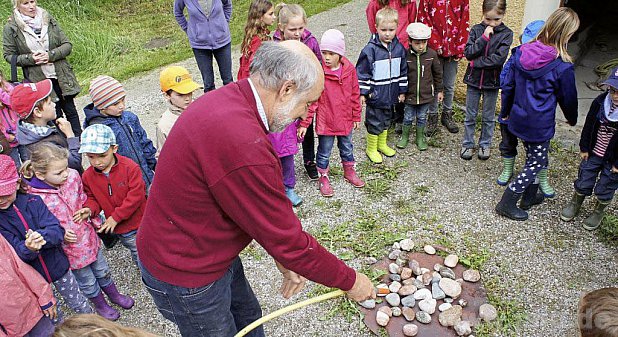 Ortsheimatpfleger Wolfgang Hopfgartner, umringt von gespannten Kindern, bereitet gerade die Salzachkiesel vor, die angeschnitten werden sollen. − Foto: Heidi Hopfgartner